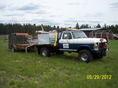 1973 Ford F-250 - This 1973 Ford F-250 flatbed truck is seen towing a trailer loaded with lumber on a cloudy day.