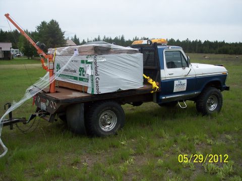 1973 Ford F-250 - Flatbed truck loaded with lumber and a boom crane, parked in a grassy field.