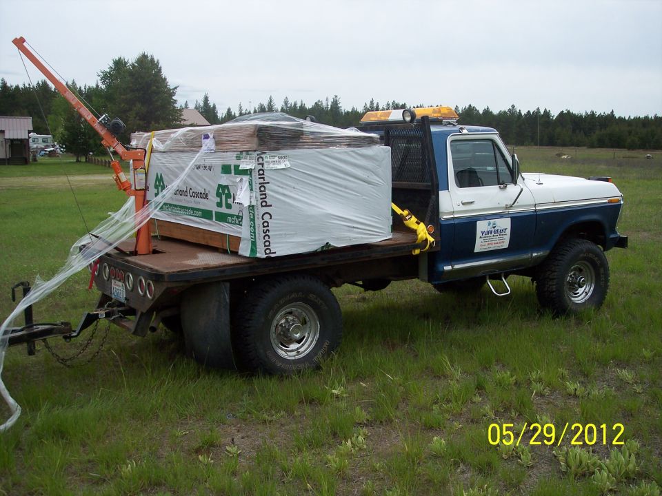 1973 Ford F-250 flatbed truck carrying lumber and a small crane