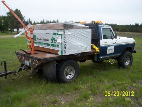 1973 Ford F-250 - A flatbed truck carries lumber and a crane, parked in a grassy area with trees in the background.
