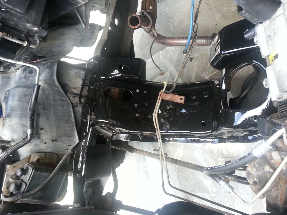 Black painted vehicle frame with engine parts and exhaust pipe. Some hoses and wires are visible