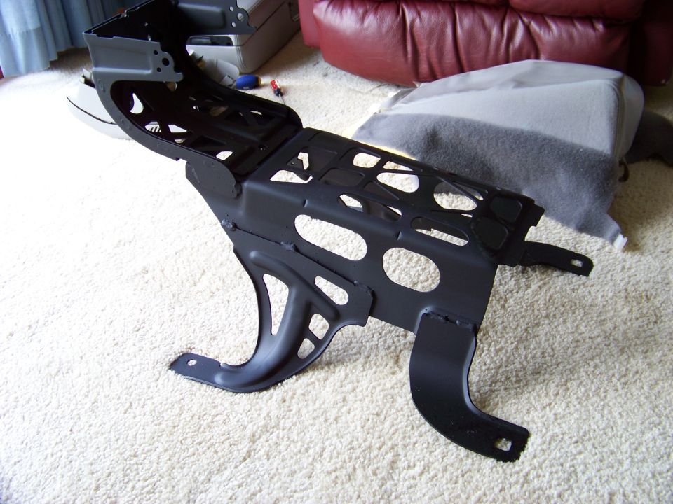Black metal car seat frame with cutouts, resting on a carpeted floor