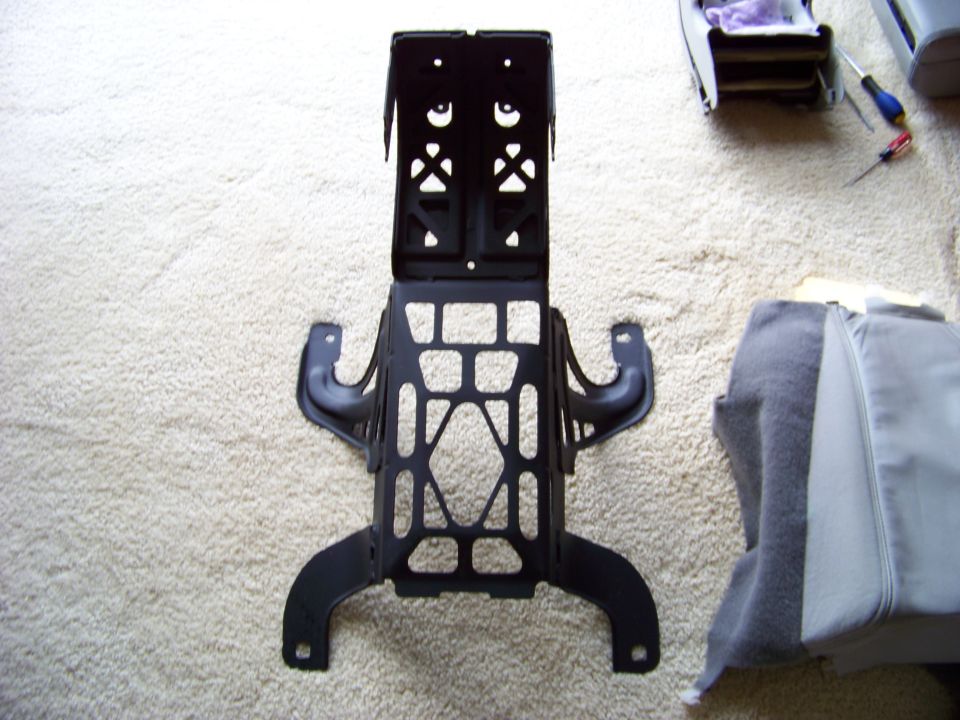 Black metal bracket with cutouts on a carpeted surface next to car seat fabric
