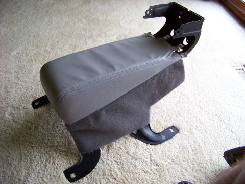 1999 Mercury Grand Marquis - A disassembled car center console armrest is shown on a carpeted surface, with visible mounting hardware.