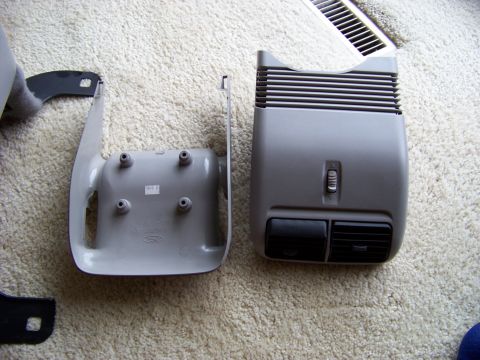 1999 Mercury Grand Marquis - Two gray plastic car interior trim pieces, one with vents and a slider, are laid out on a carpeted floor.
