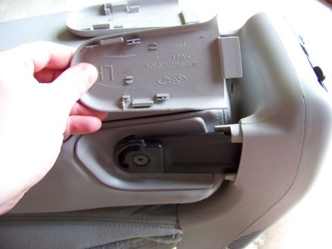 1999 Mercury Grand Marquis - A hand holds a gray plastic cover revealing a Ford part number on the underside, likely from a car seat interior.