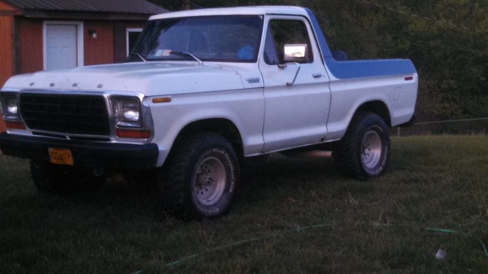 White Ford Bronco with blue top parked on grass. Yellow license plate visible