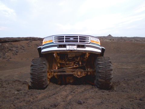1996 Ford Bronco - Modified Ford F-Series truck with oversized tires sits in a dirt terrain under a cloudy sky.