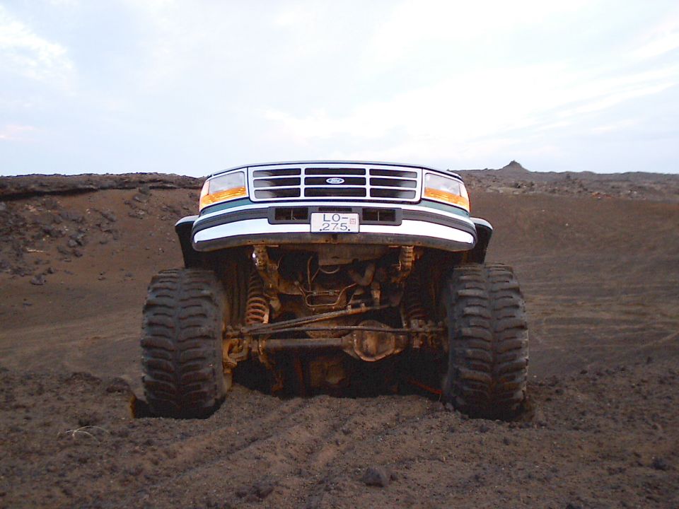 White lifted Ford truck front, low angle showing axle, steering and big tires in dark dirt