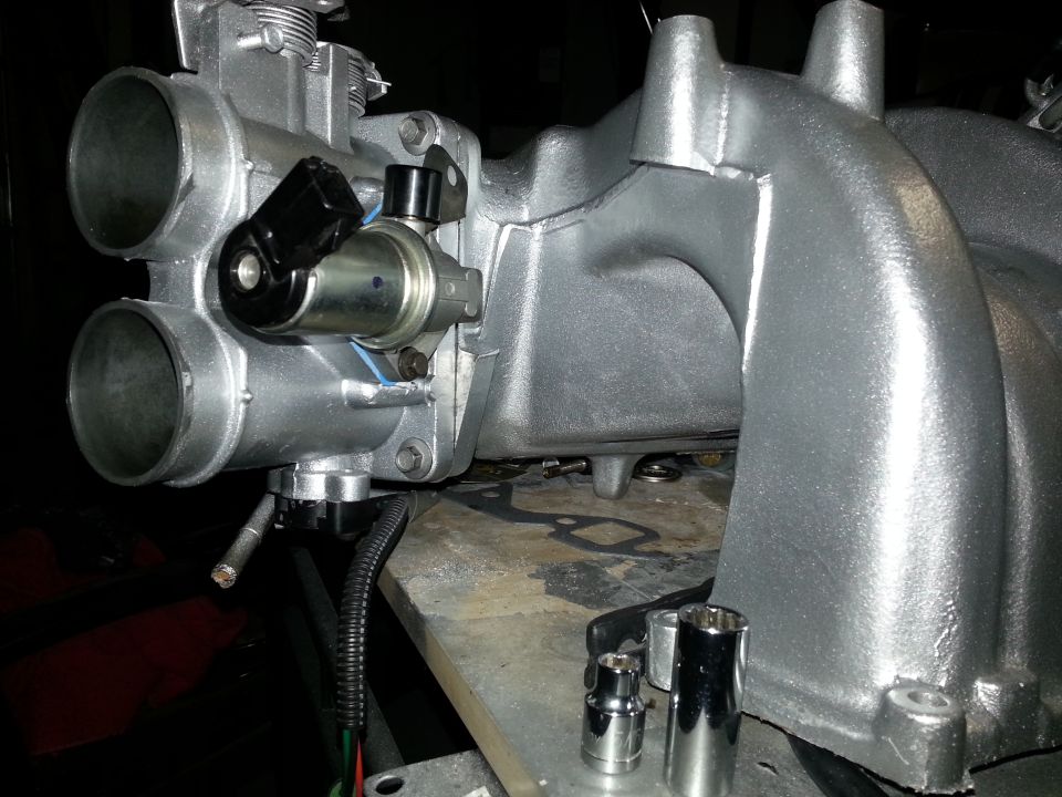 Silver throttle body and intake manifold with black sensor, on a workbench with sockets