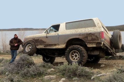 1989 Ford Bronco - A man poses with a mud-covered Ford Bronco near a body of water.