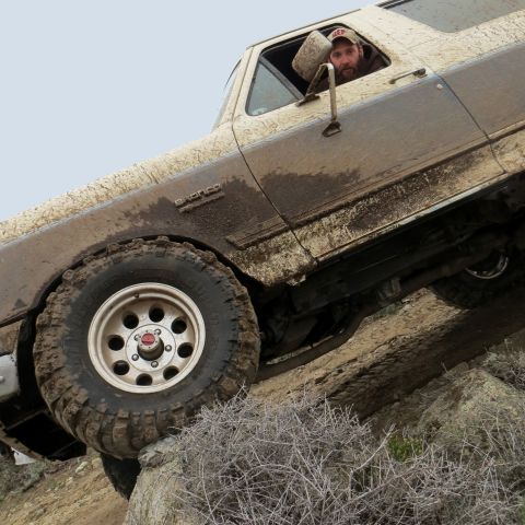 1989 Ford Bronco - A muddy 1987 Ford Bronco navigates a challenging off-road terrain with a driver at the wheel.