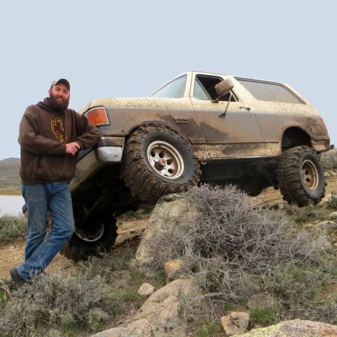1989 Ford Bronco - A man poses with a muddy 1989 Ford Bronco navigating rocky terrain.