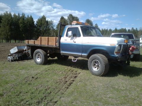 1973 Ford F-250 - A blue and white 1973 Ford F-250 flatbed truck is parked on a field with a planter attached to its rear.
