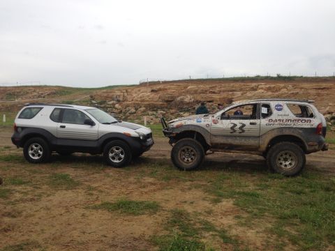 1999 Isuzu Vehicross - Two Isuzu Vehicross SUVs are parked on a dirt track, one stock and one modified for off-road racing.
