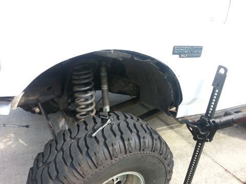 1992 Ford Bronco - A white 1992 Ford Bronco XLT is shown with its front suspension, including the coil spring and shock absorber, exposed for service.