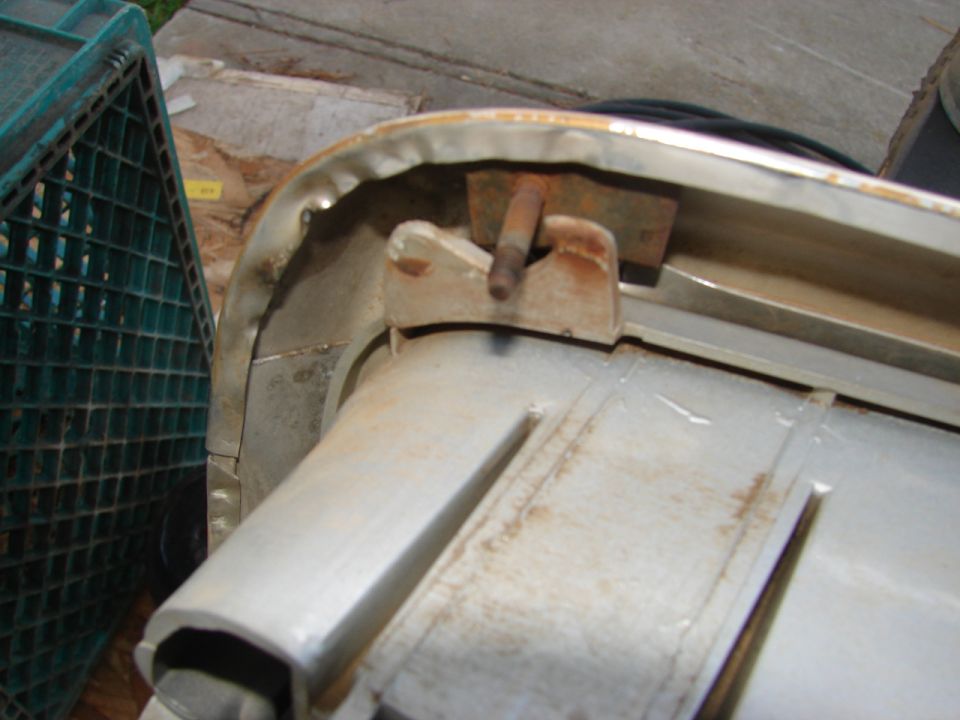 Rusted metal bracket attached to a white car part, with a green plastic crate in the background