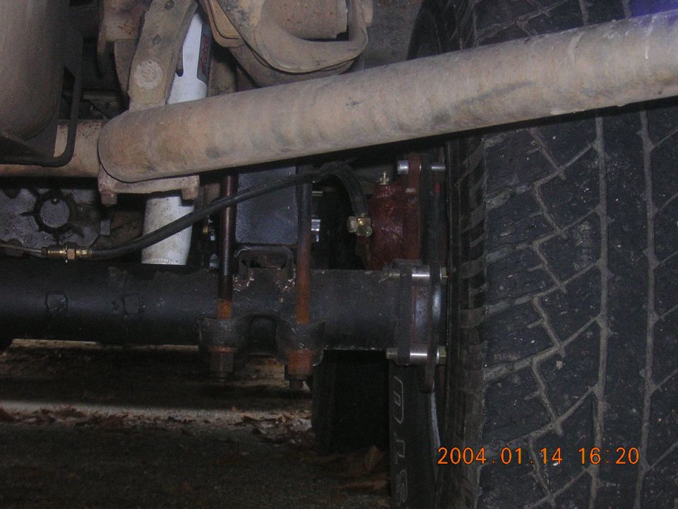 Close-up of a vehicle's rear axle, leaf spring, shock absorber, and tire. Date stamp reads 2004 01 14