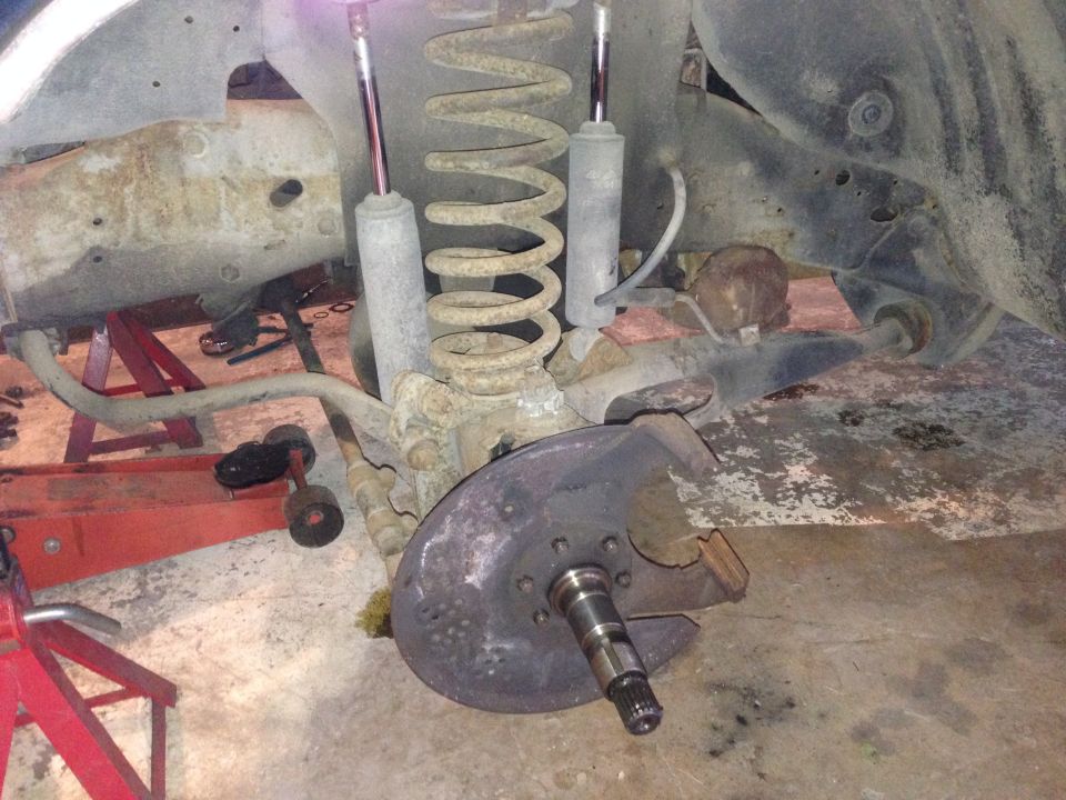 close-up of a vehicle's front suspension and brake rotor assembly, with springs and shocks visible