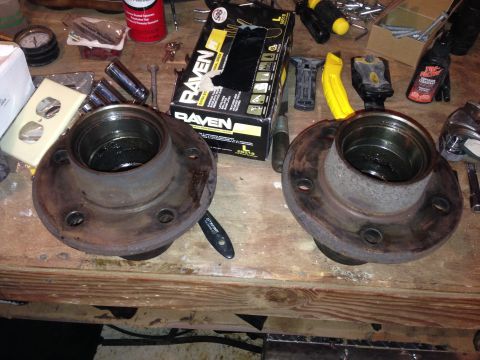 1990 Ford Bronco - Two used brake rotors and hubs sit on a workbench next to a box of Raven gloves and various tools.