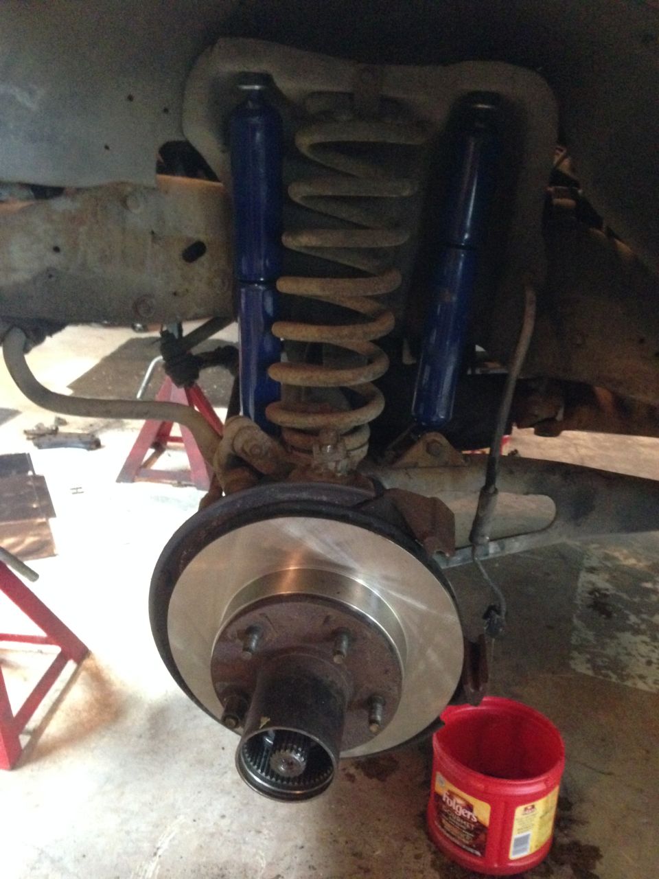 close-up of a vehicle's front brake rotor and suspension with blue shocks