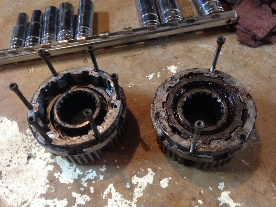 Two used automatic locking hubs with bolts, resting on a concrete floor next to a socket wrench set