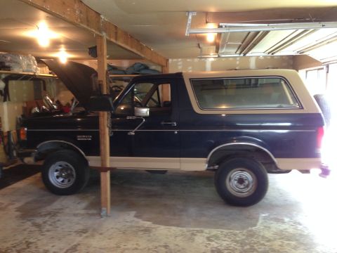 1990 Ford Bronco - A side view of a Ford Bronco, likely from the late 1980s, is parked inside a garage with its hood open.