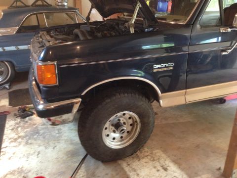 1990 Ford Bronco - A dark blue Ford Bronco with tan lower body panels is parked in a garage with its hood open.
