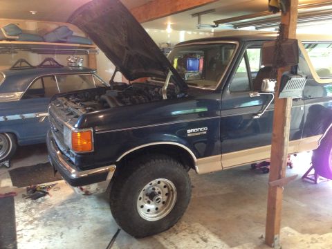 1990 Ford Bronco - A dark blue 1990 Ford Bronco is parked in a garage with its hood open, alongside another blue vehicle.