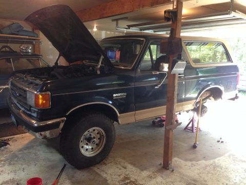 1990 Ford Bronco - Ford Bronco undergoing maintenance in a garage, with the hood up and wheels off.