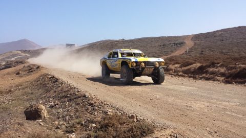 1996 Ford Bronco - A yellow off-road race car navigates a dusty track under a clear blue sky.