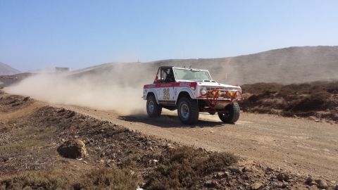 1996 Ford Bronco - A vintage Ford Bronco races off-road, leaving a trail of dust in its wake under a clear blue sky.