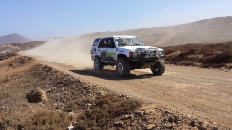 1996 Ford Bronco - Modified SUV races off-road, kicking up a large dust cloud on a sunny day.