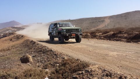 1996 Ford Bronco - An off-road SUV navigates a dusty track under a clear blue sky.