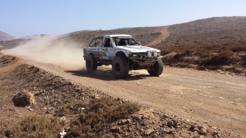 1996 Ford Bronco - A white off-road truck races down a dusty track, kicking up a cloud of dust behind it.