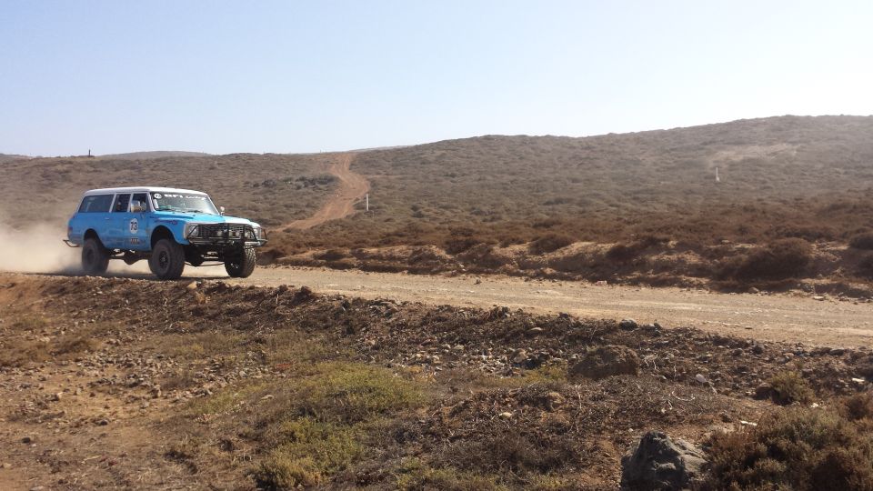 Blue off-road truck kicking up dust on a dirt road in a dry, hilly landscape