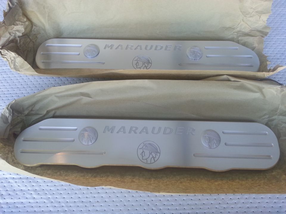 Two aluminum Marauder branded coil covers, one on top of the other, wrapped in paper