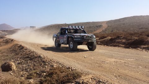 1996 Ford Bronco - A modified off-road truck races down a dusty desert track, leaving a trail of dust behind it.