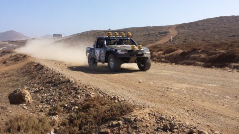 1996 Ford Bronco - A race truck navigates a dusty desert terrain on a sunny day.