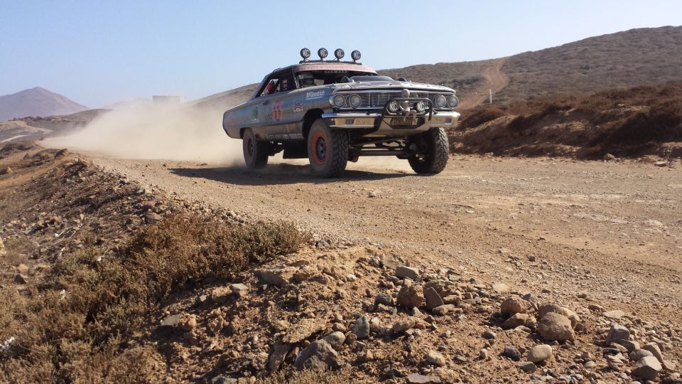 Old sedan modified for off-road racing, kicking up dust on a dirt track