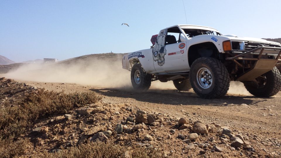 White off-road truck kicking up dust on a dirt track, with a skull graphic on the door