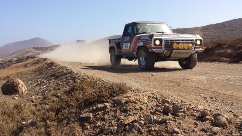 1996 Ford Bronco - A vintage Ford pickup truck competes in an off-road race, its tires kicking up a cloud of dust on the arid terrain.