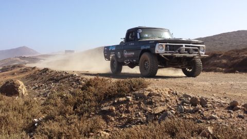 1996 Ford Bronco - This modified pickup truck is racing on a dusty desert terrain under a clear blue sky.