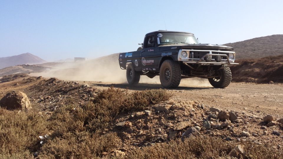 Black pickup truck with off-road tires and bumper driving on a dirt road, kicking up dust