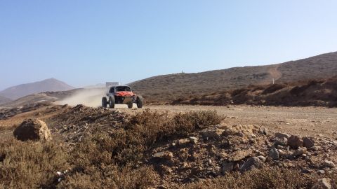 1996 Ford Bronco - An off-road buggy races along a dusty track in a desert landscape under a clear blue sky.