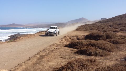 1996 Ford Bronco - Off-road buggy races along a coastal dirt track, creating a dust cloud.