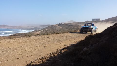 1996 Ford Bronco - A blue off-road truck races along a dusty coastal road.