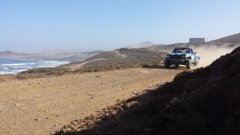 Blue off-road truck kicking up dust on a dirt road near the ocean