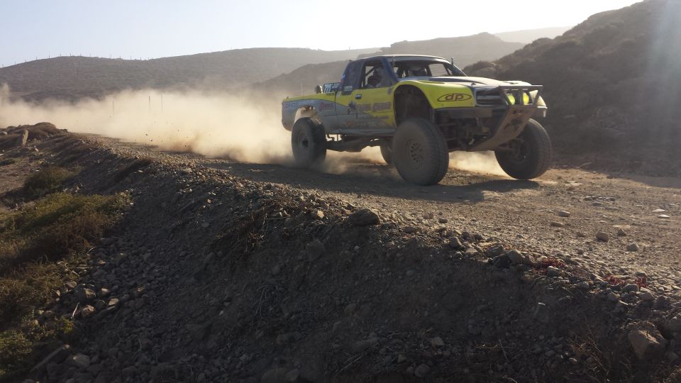 Yellow off-road truck with large tires kicking up dust on a dirt road