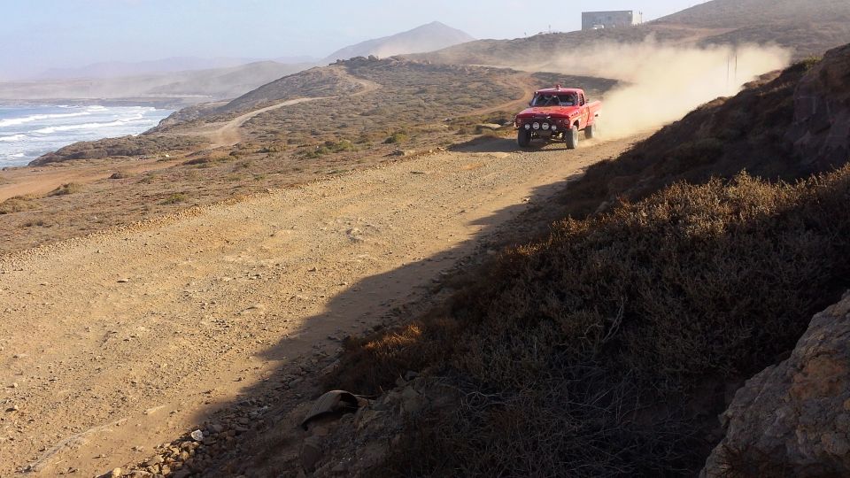Red pickup truck kicking up dust on a dirt road near the ocean